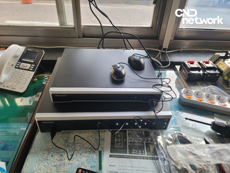 경비실 책상 위 나란히 놓인 HIKVISION NVR 2대, 마우스와 케이블이 연결된 신규 장비 설치 완료 사진